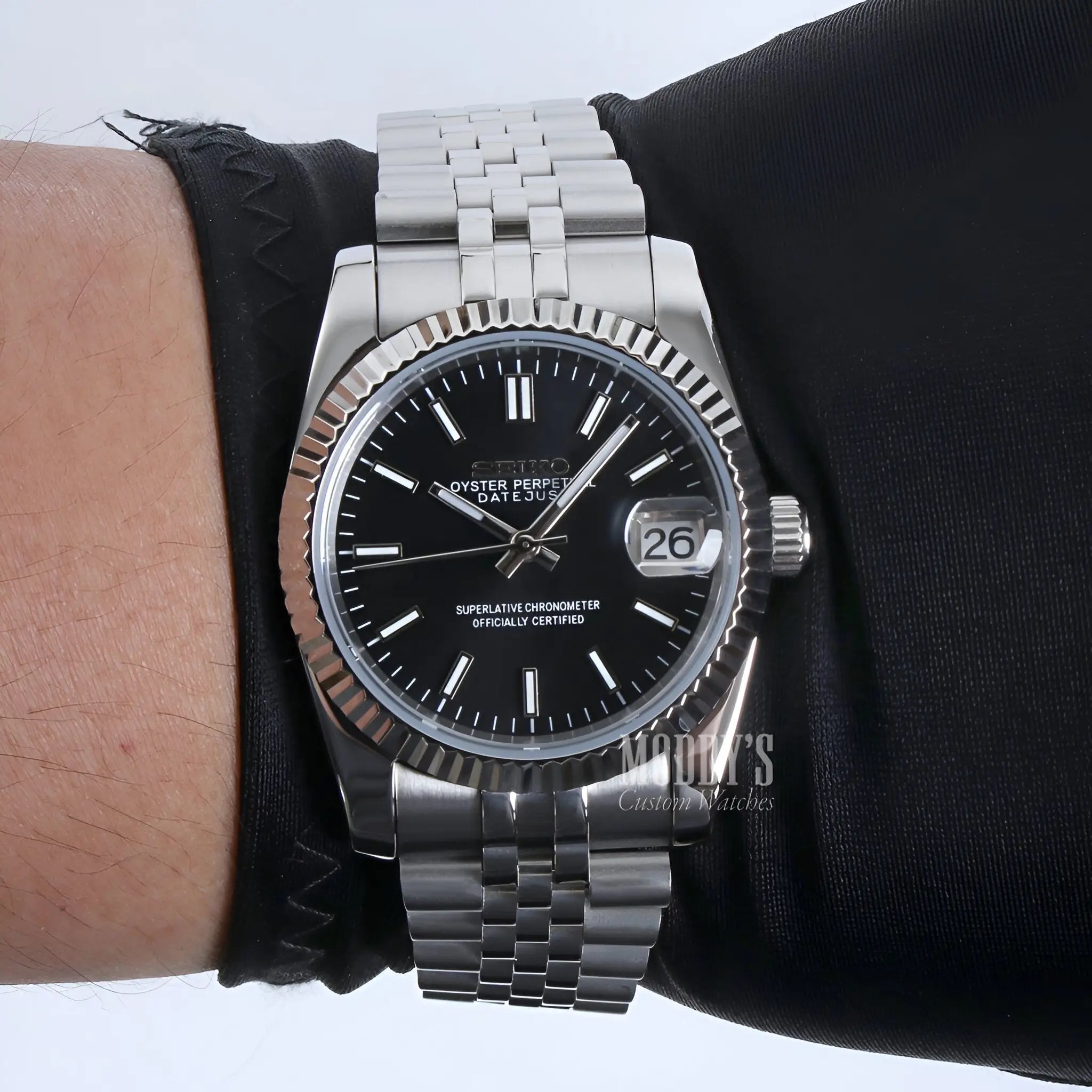 black dial stainless steel Seiko mod watch with fluted bezel and jubilee bracelet, angled close-up on wooden surface
